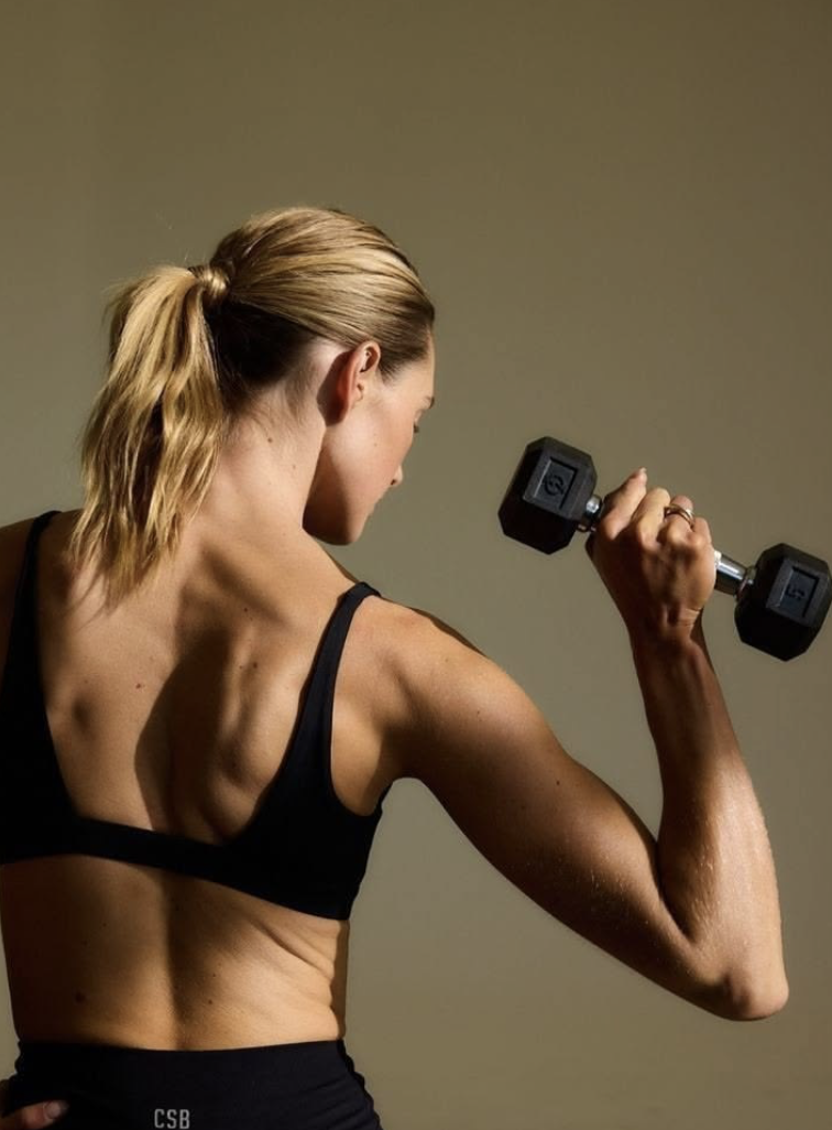Woman seen from behind training her arm with a dumbbell